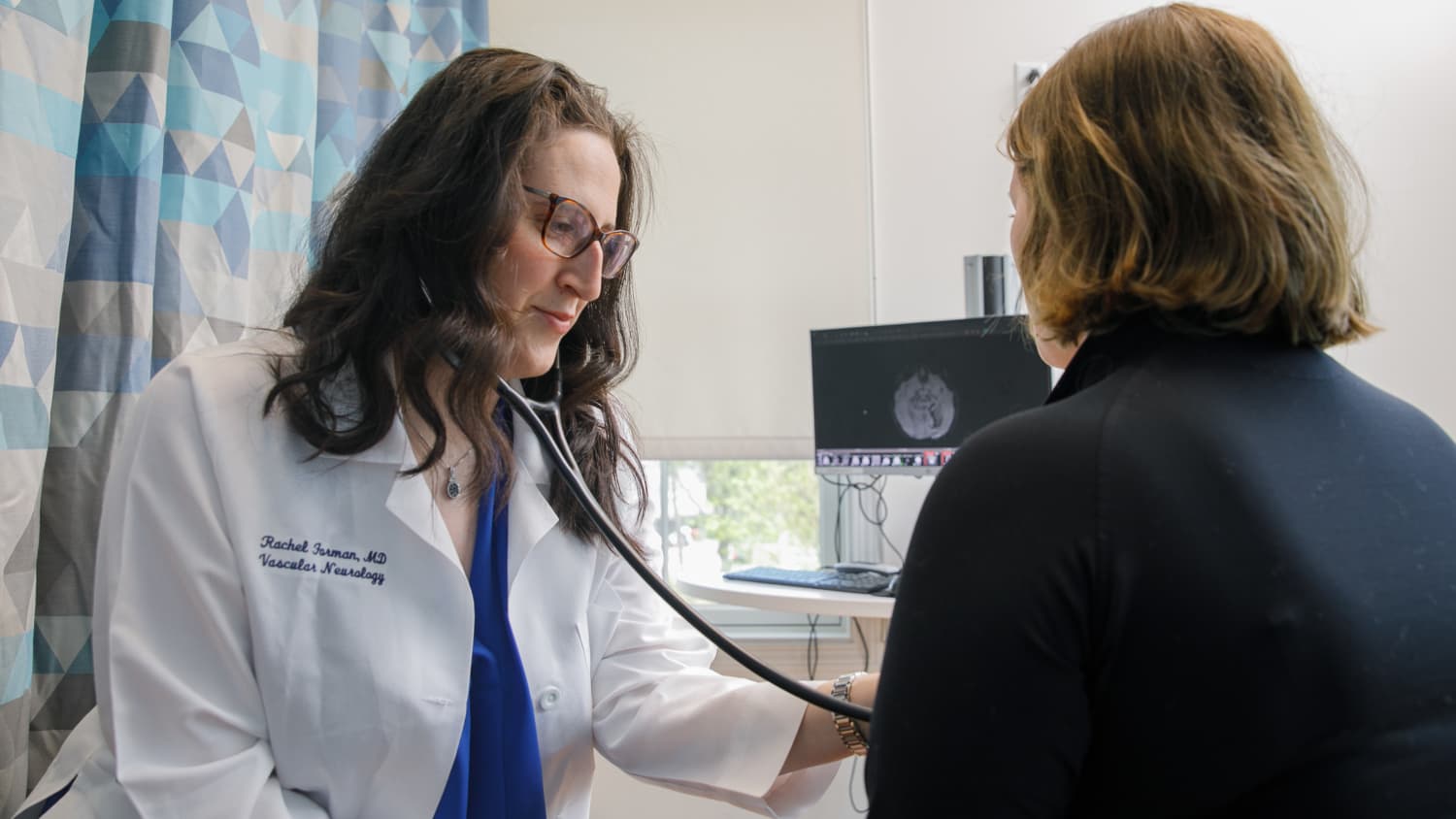 A Yale Medicine physician who specializes in stroke, listens to a female patient's heart in the office. h a female patient in the office,