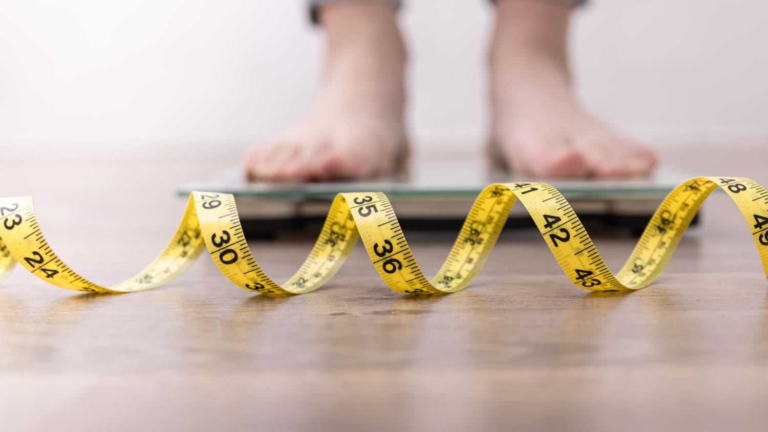 Person standing on a scale with tape measure unfurled on floor.