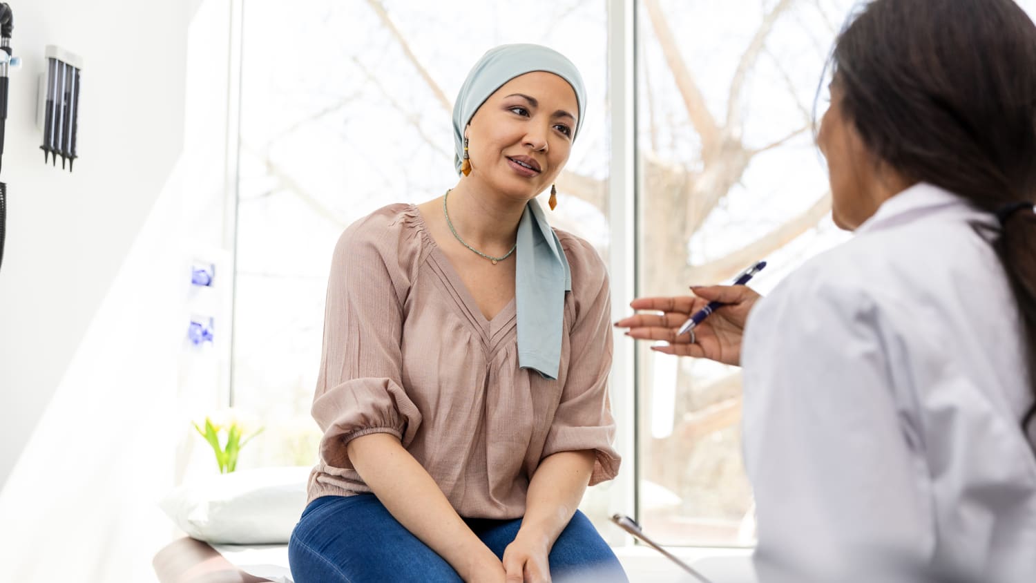 A woman wearing a headscarf talks to her cancer doctor in an exam room. 