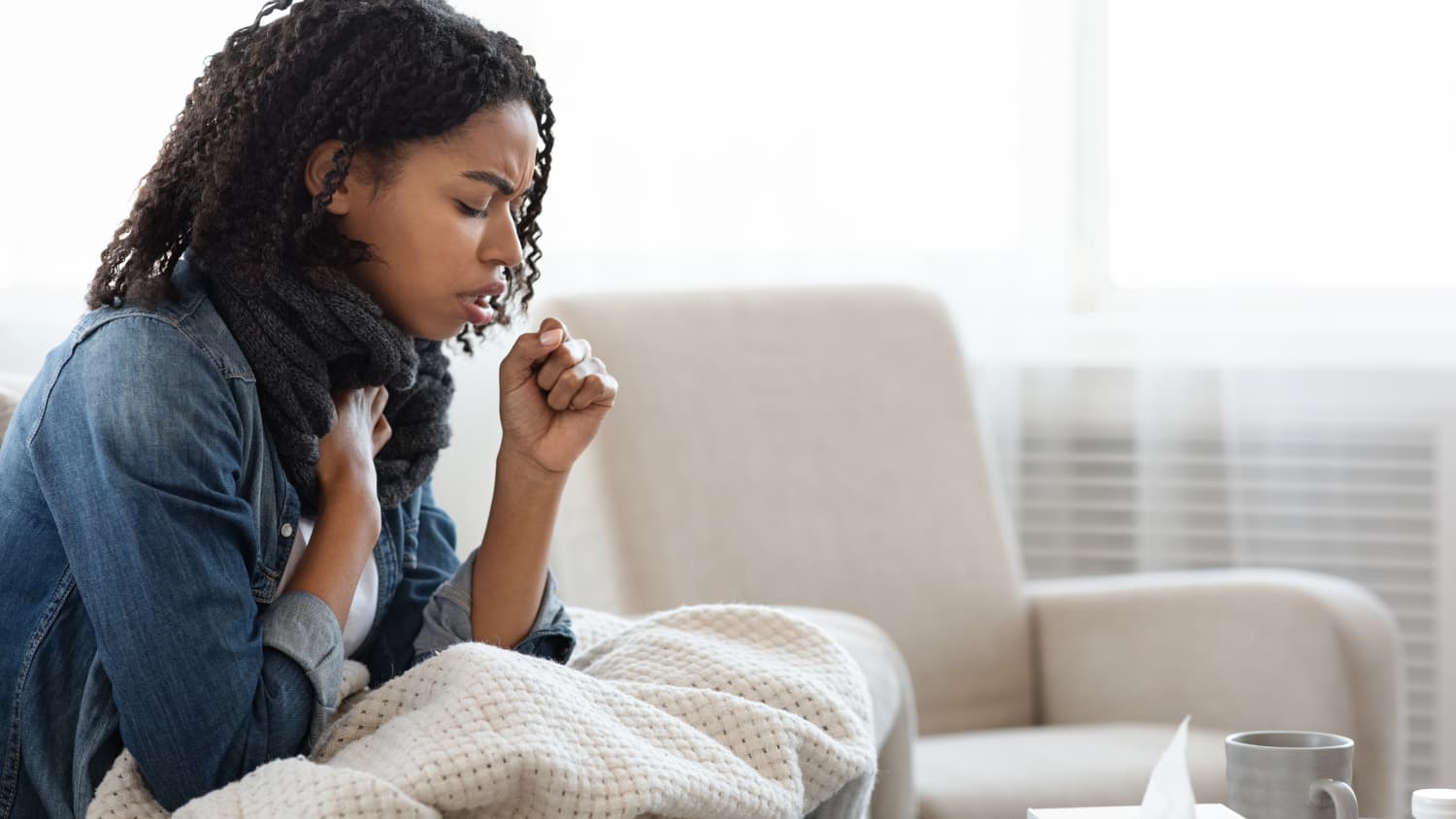 young woman with walking pneumonia on a couch coughing