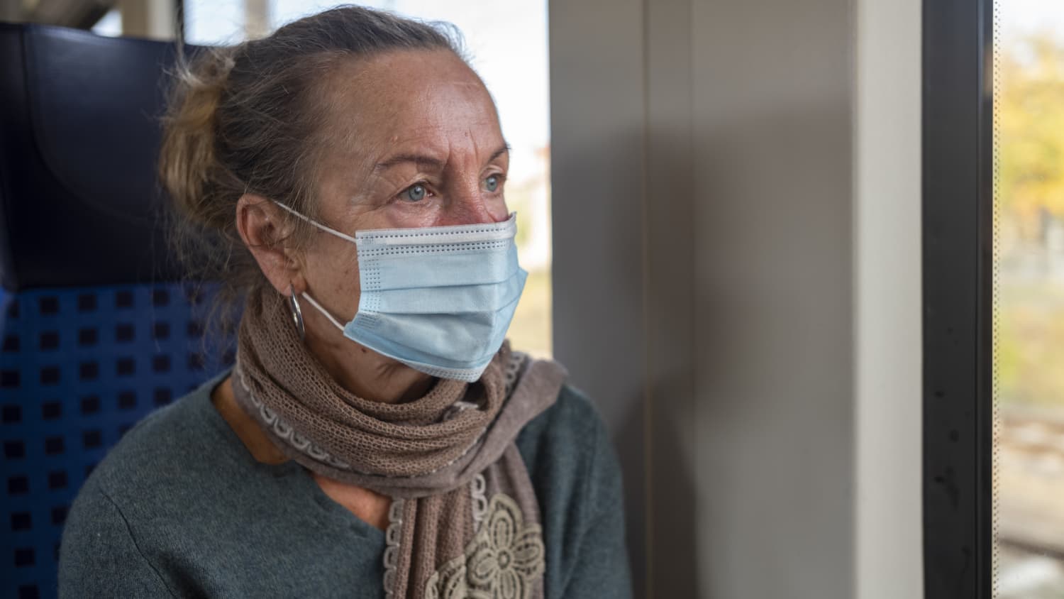 older woman practicing strategic masking on a train to protect against COVID