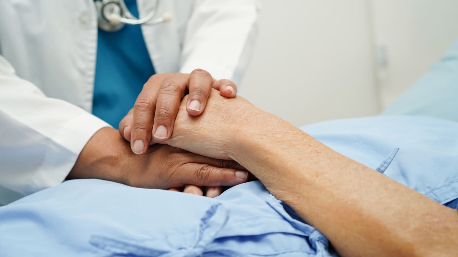 A doctor hold's a palliative care patient's hand in a hospital. 