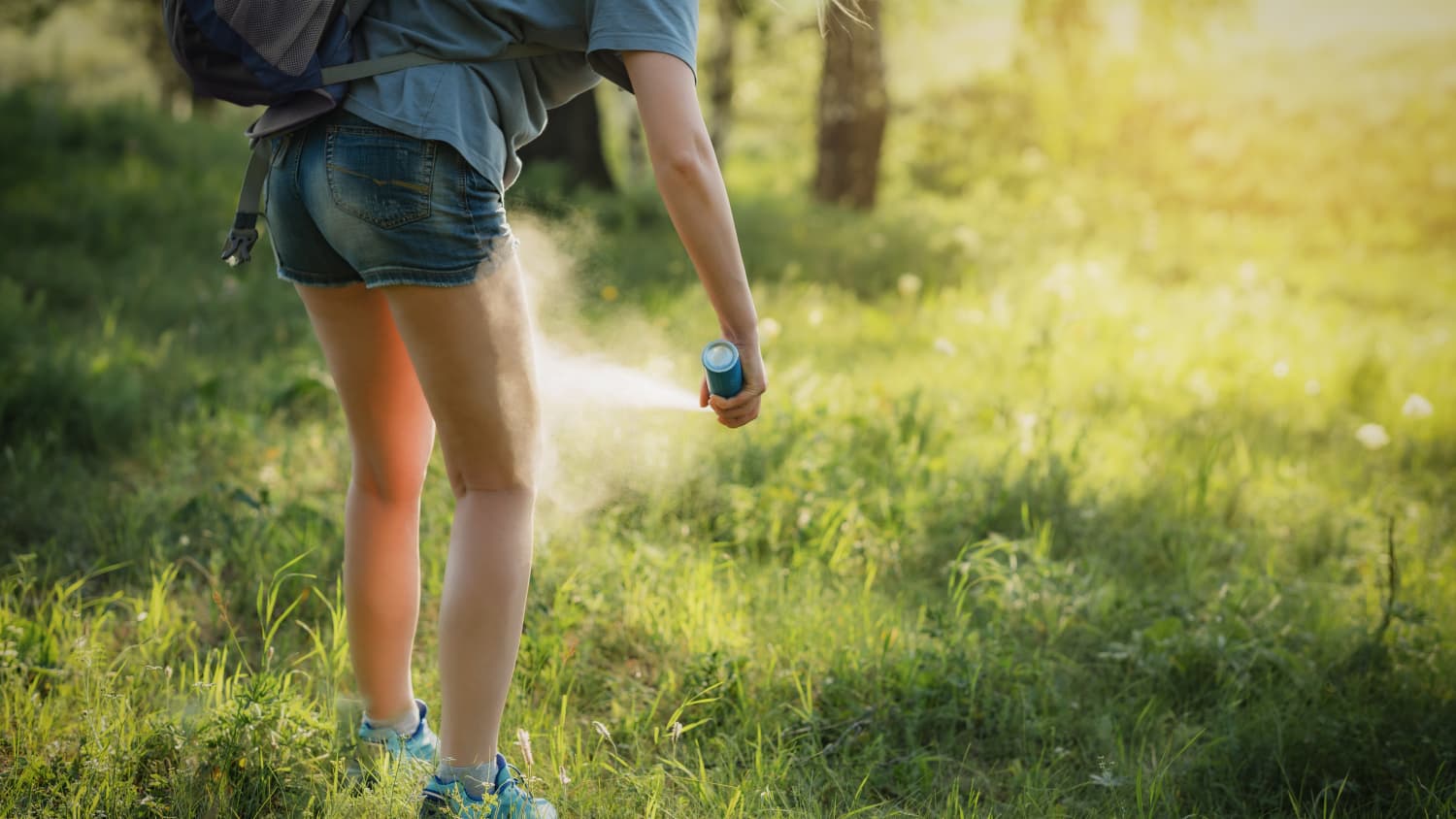 A girl standing in the woods applies insect repellent to protect against ticks, bites from which can cause alpha-gal syndrome. 