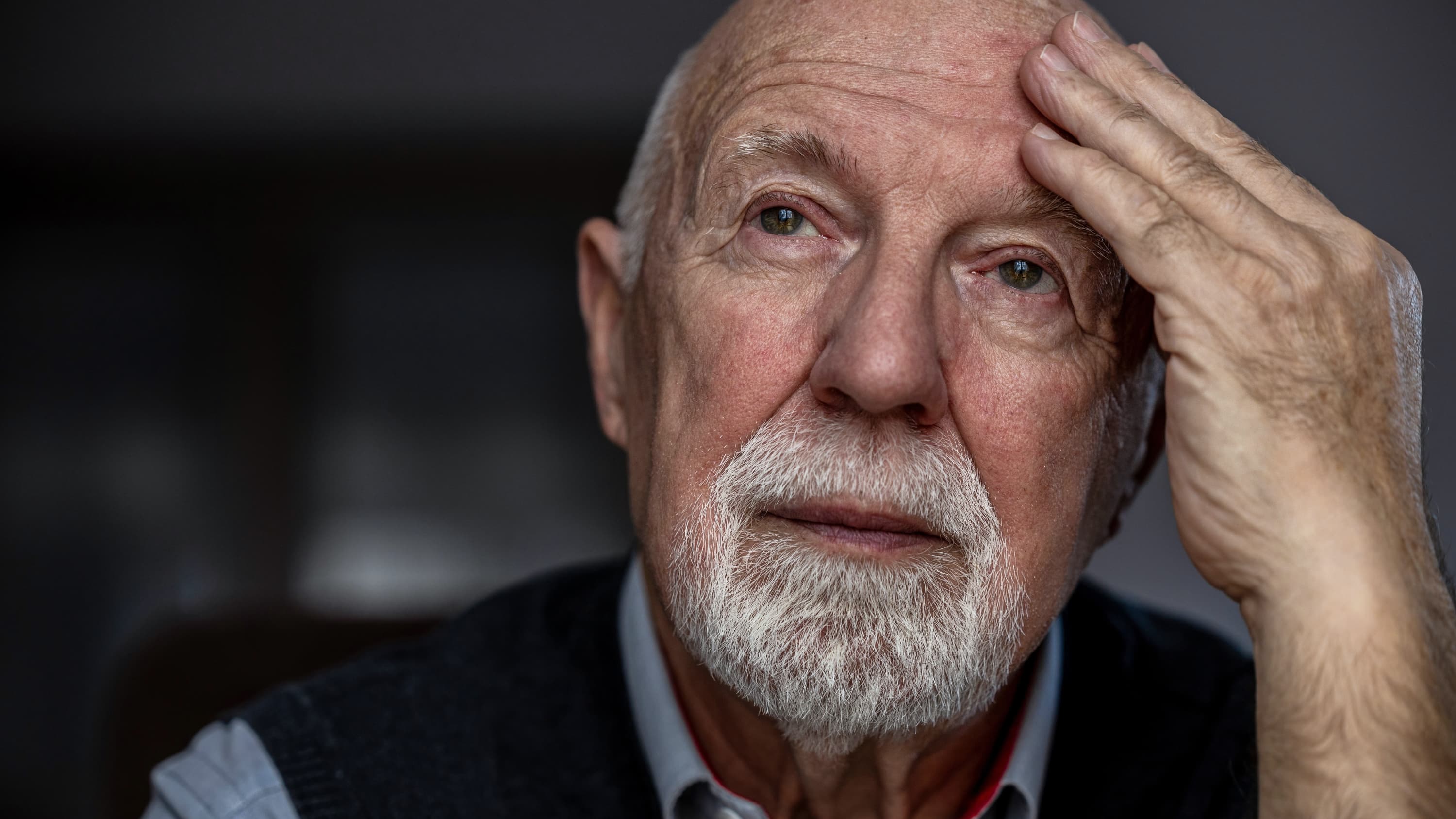 An older man with Alzheimer's disease places his hand on his forehead. 