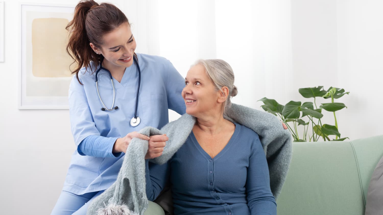 A nurse puts a blanket over the shoulder of a female palliative care patient.