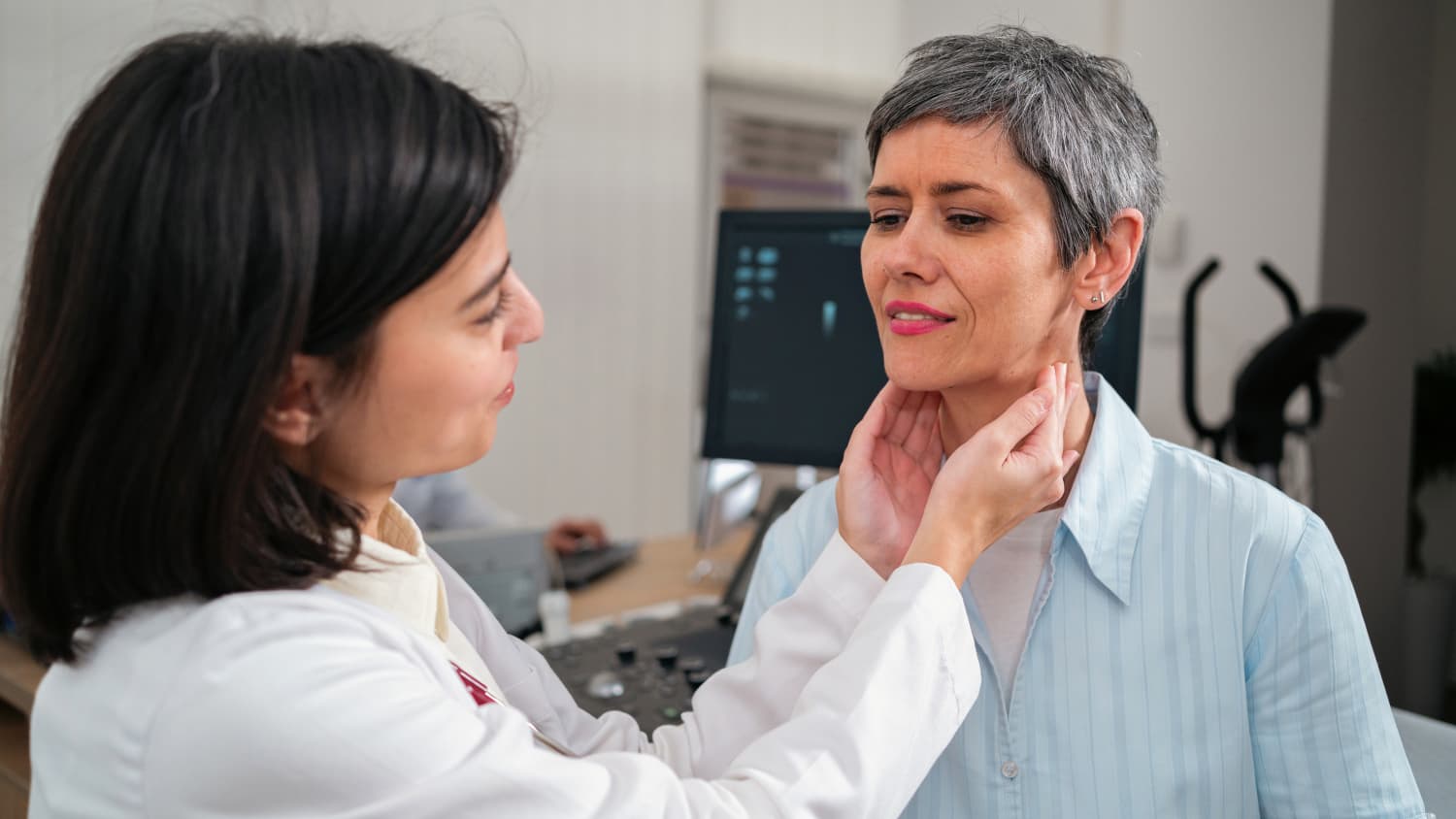 Doctor palpates a middle-aged woman's neck to check for a lump or swelling that could be a sign of thyroid cancer.