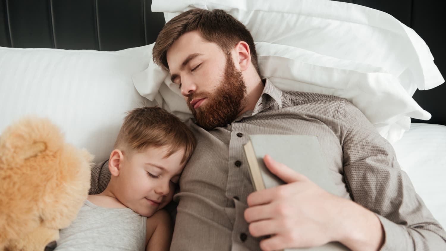image-of-boy-sleeping-at-home-in-bed-near-toy-with-his-bearded-father-holding-book-SBI-302832596