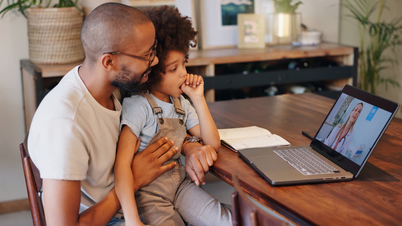 A father and daughter talk to a medical provider on a laptop. 