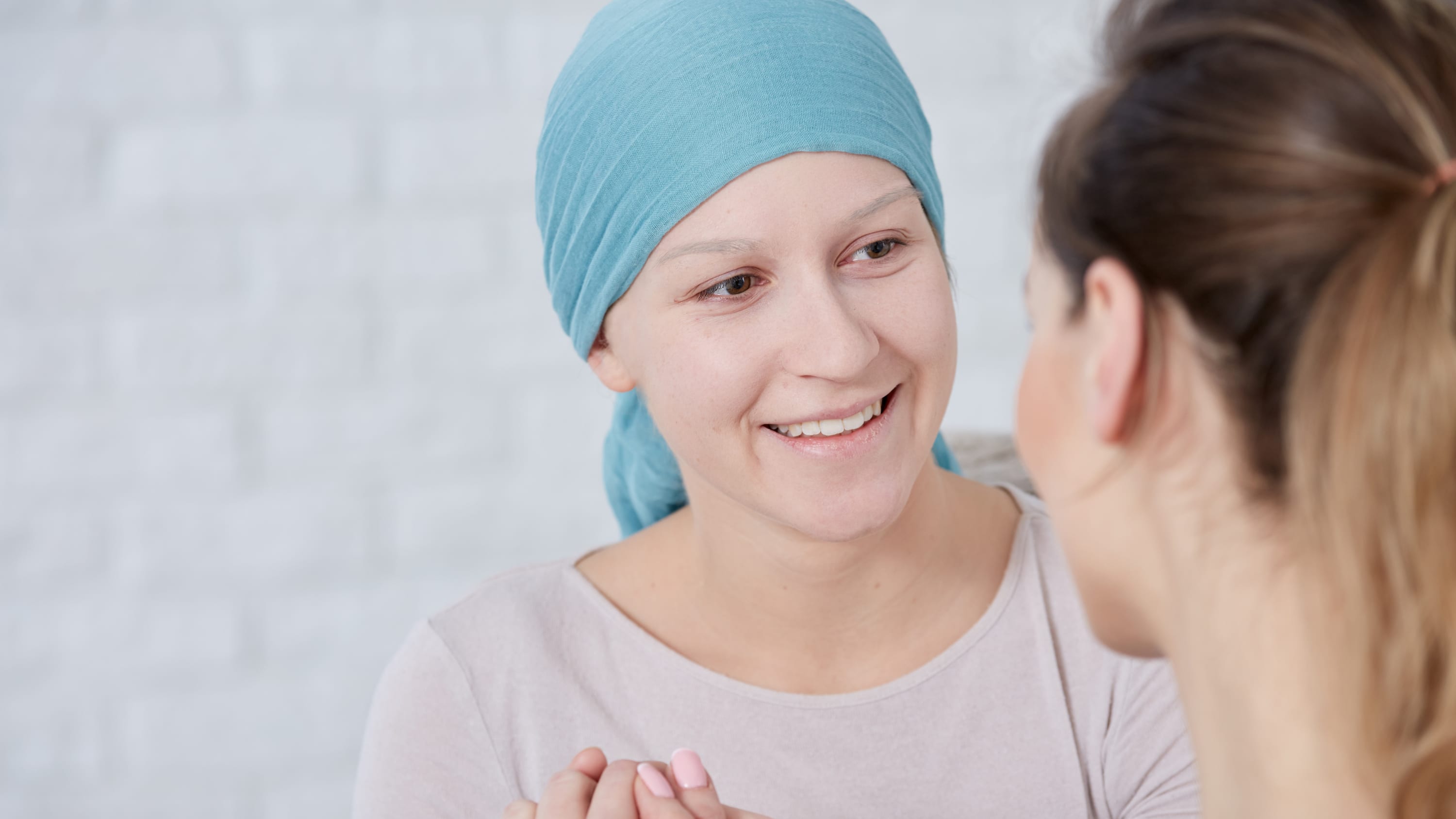 A woman in a head wrap smiles as she converses with a woman with a pony tail.