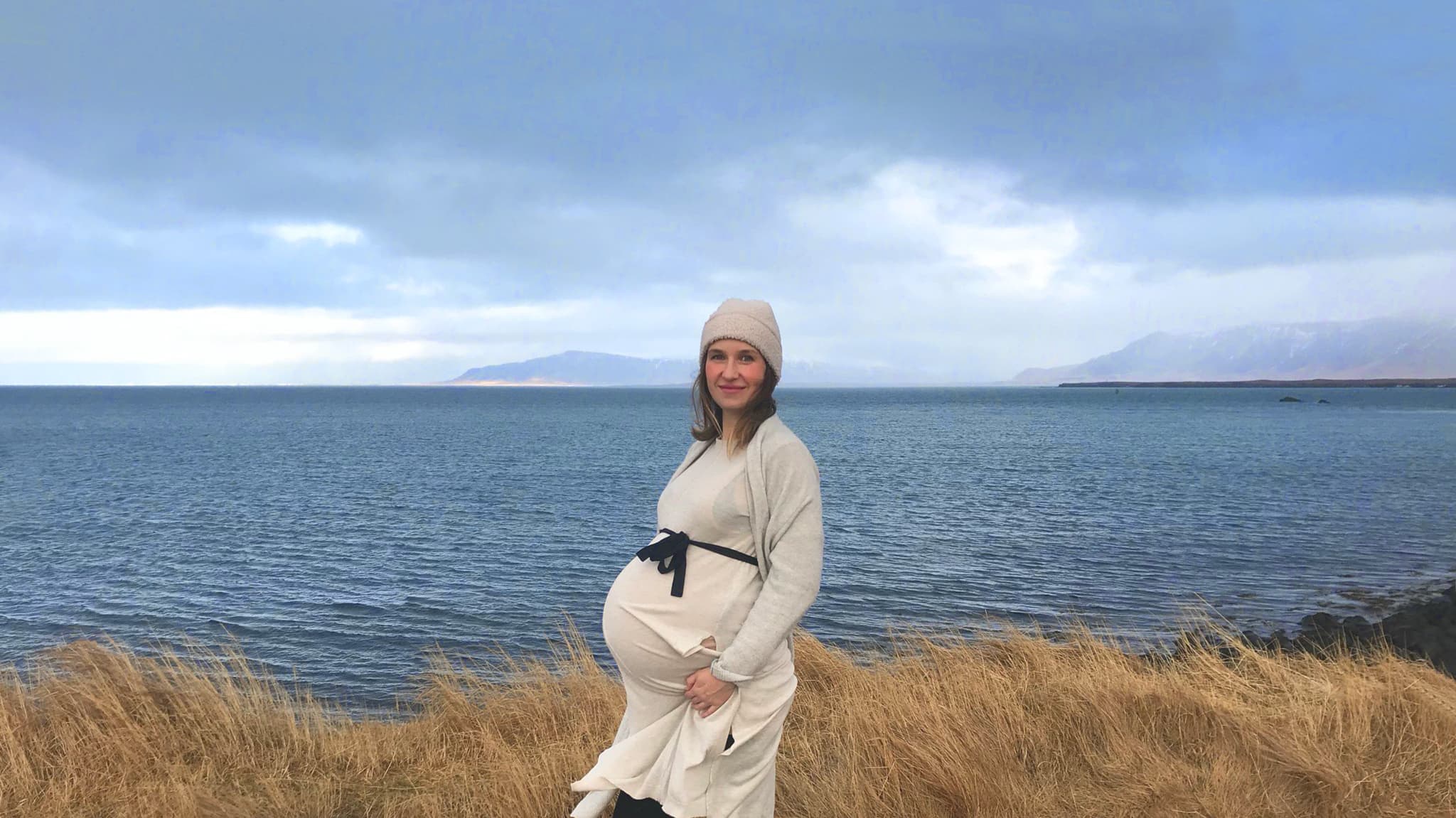 A pregnant woman stands in front of Icelandic scenery.