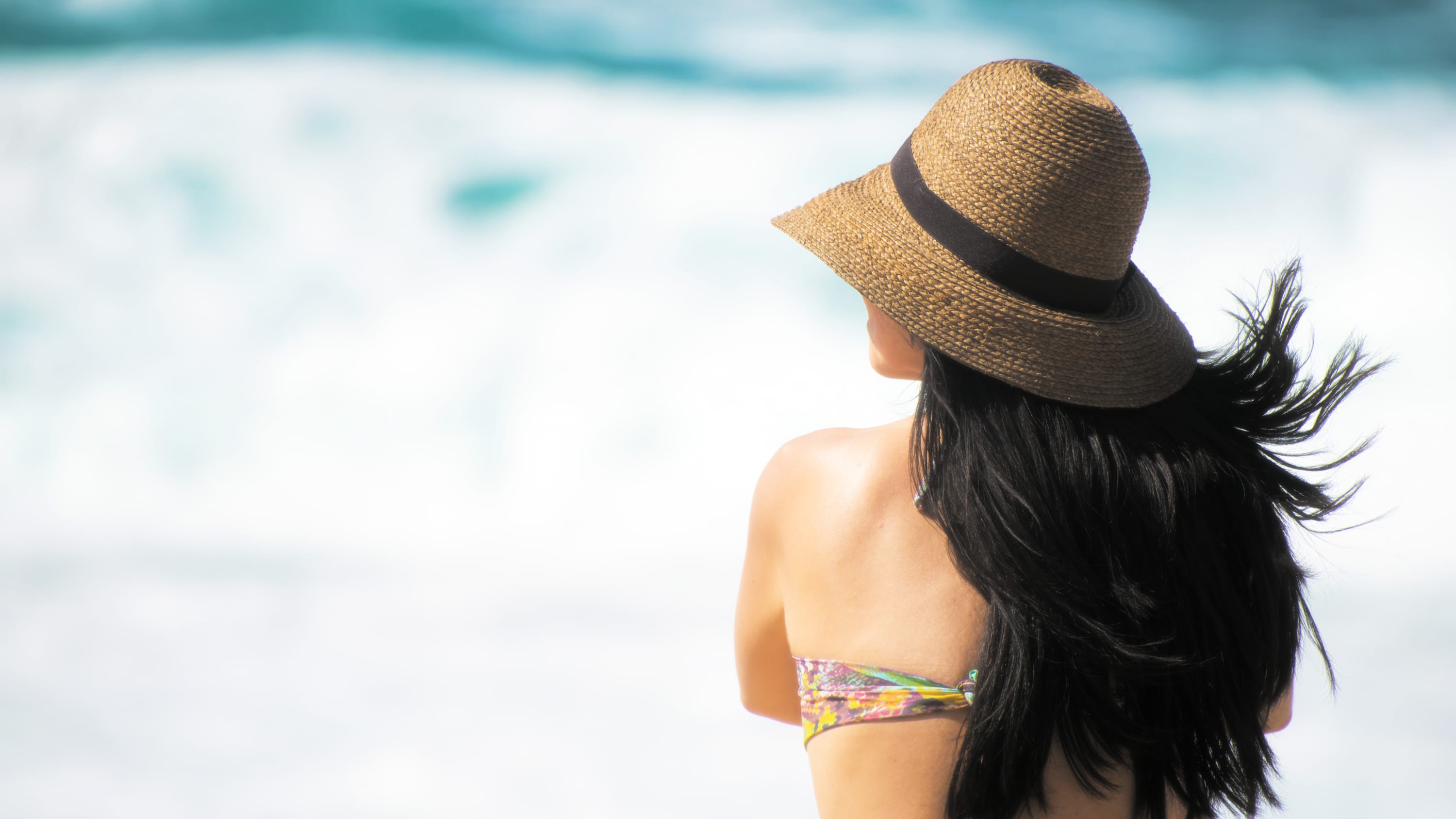 Woman on beach with long dark hair wearing hat.