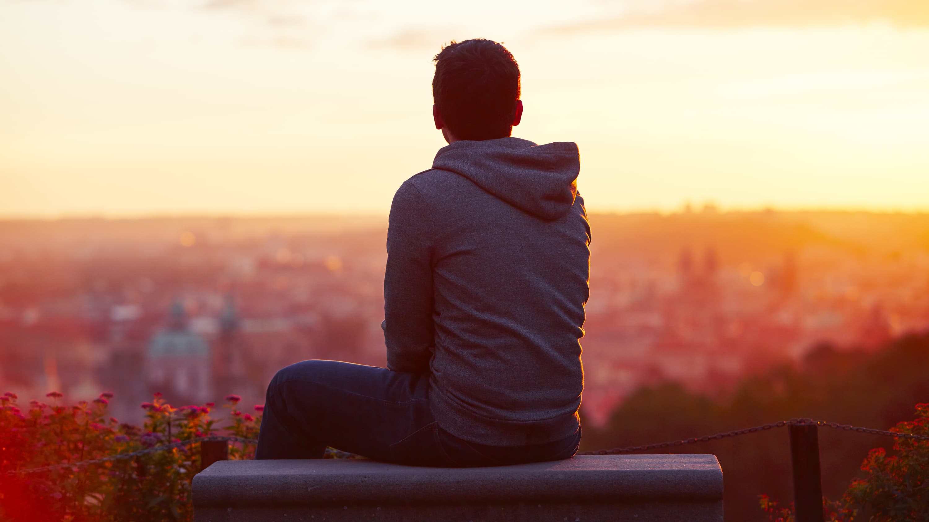young man sitting on a bench looking out over a city, worried and stress about COVID-19